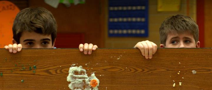 still from Incident at Public School 173 - 2 boys peering over food-stained table