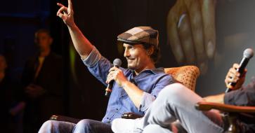 With his arm up in a "hook 'em" hand sign, Matthew McConaughey sits in an armchair during the Q&A portion of the screening event
