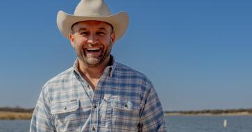Chet Garner stands and smiles in front of a lake