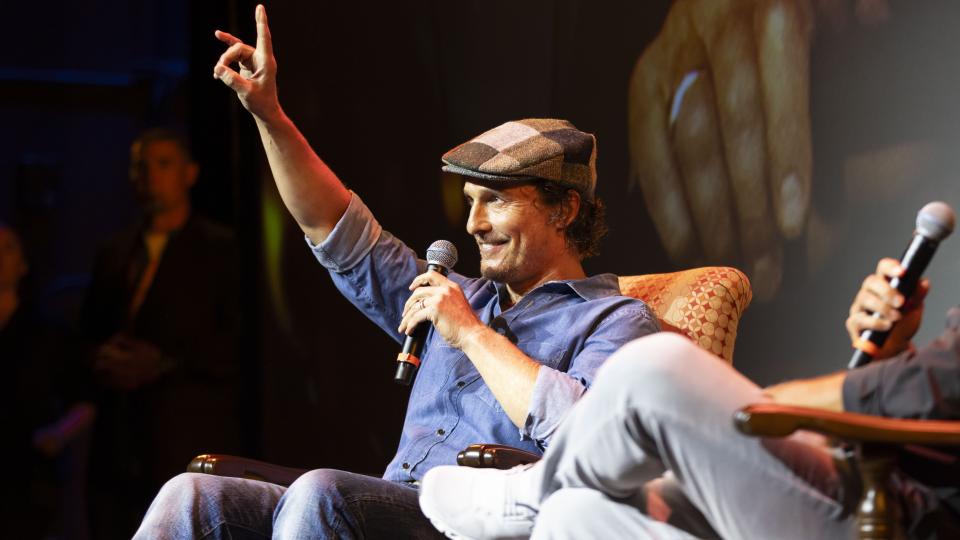 With his arm up in a "hook 'em" hand sign, Matthew McConaughey sits in an armchair during the Q&A portion of the screening event