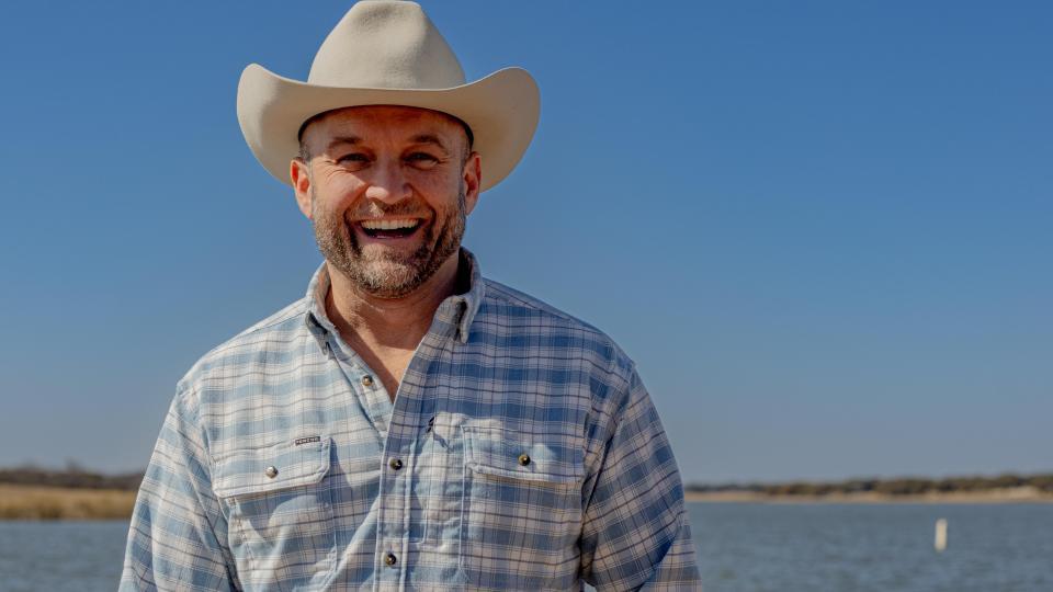 Chet Garner stands and smiles in front of a lake