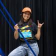 A student stands on a production ladder in an RTF t-shirt and baseball cap with her hand in a "hook 'em" sign.