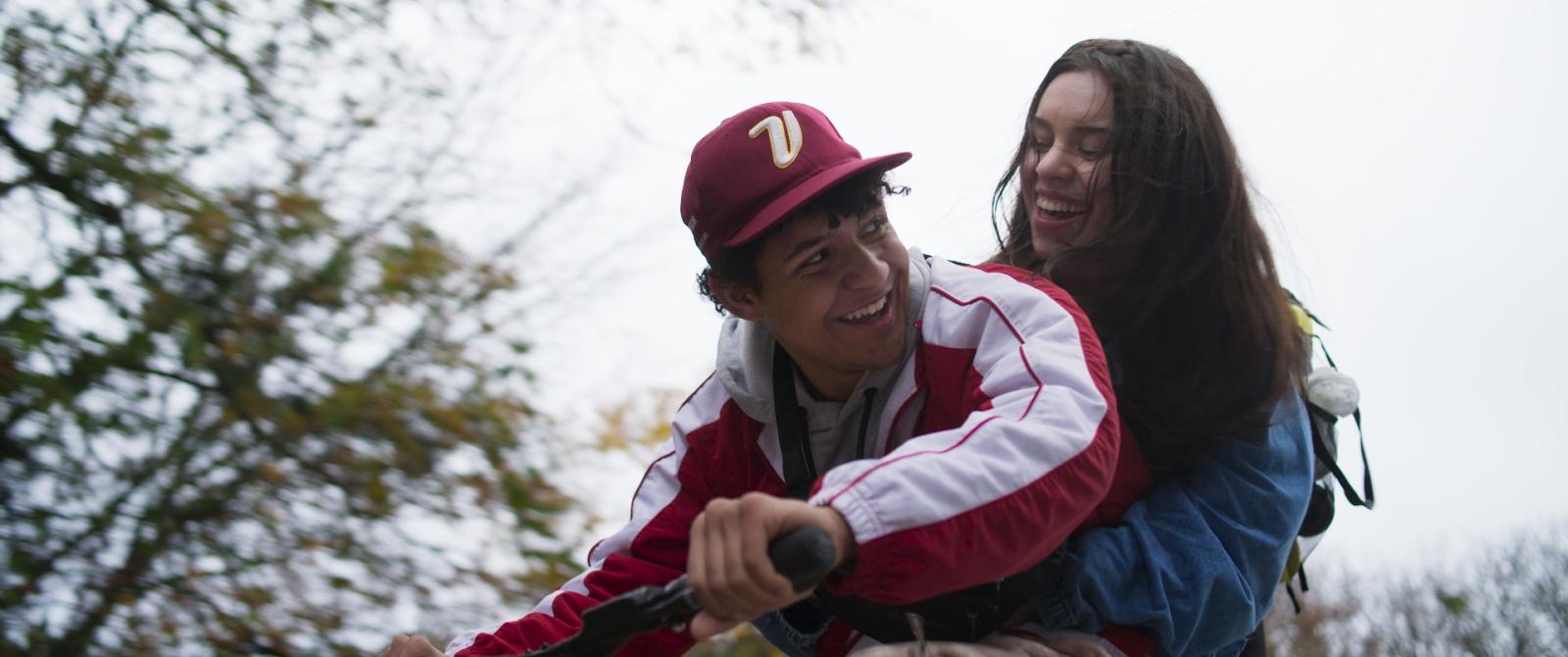 A still of Camilo Montoya's Film, "Grin" showing two people riding a bike and laughing.