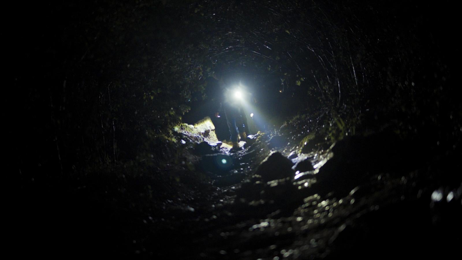 A still of Noah Hyo Won Seo's Film, "Korean Calls, Chinese Phone" showing someone illuminating a dark trail with a flashlight. 