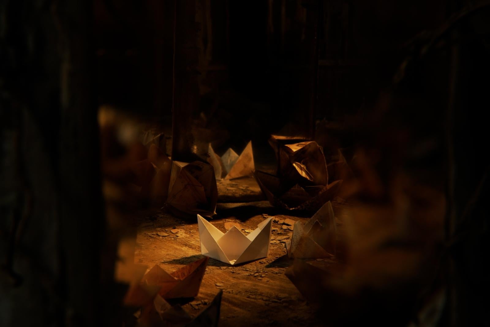 A still of Mauricio Hernandez Serrano's film "CHABACANO" showing paper origami in a dark room illuminated by a spotlight. 