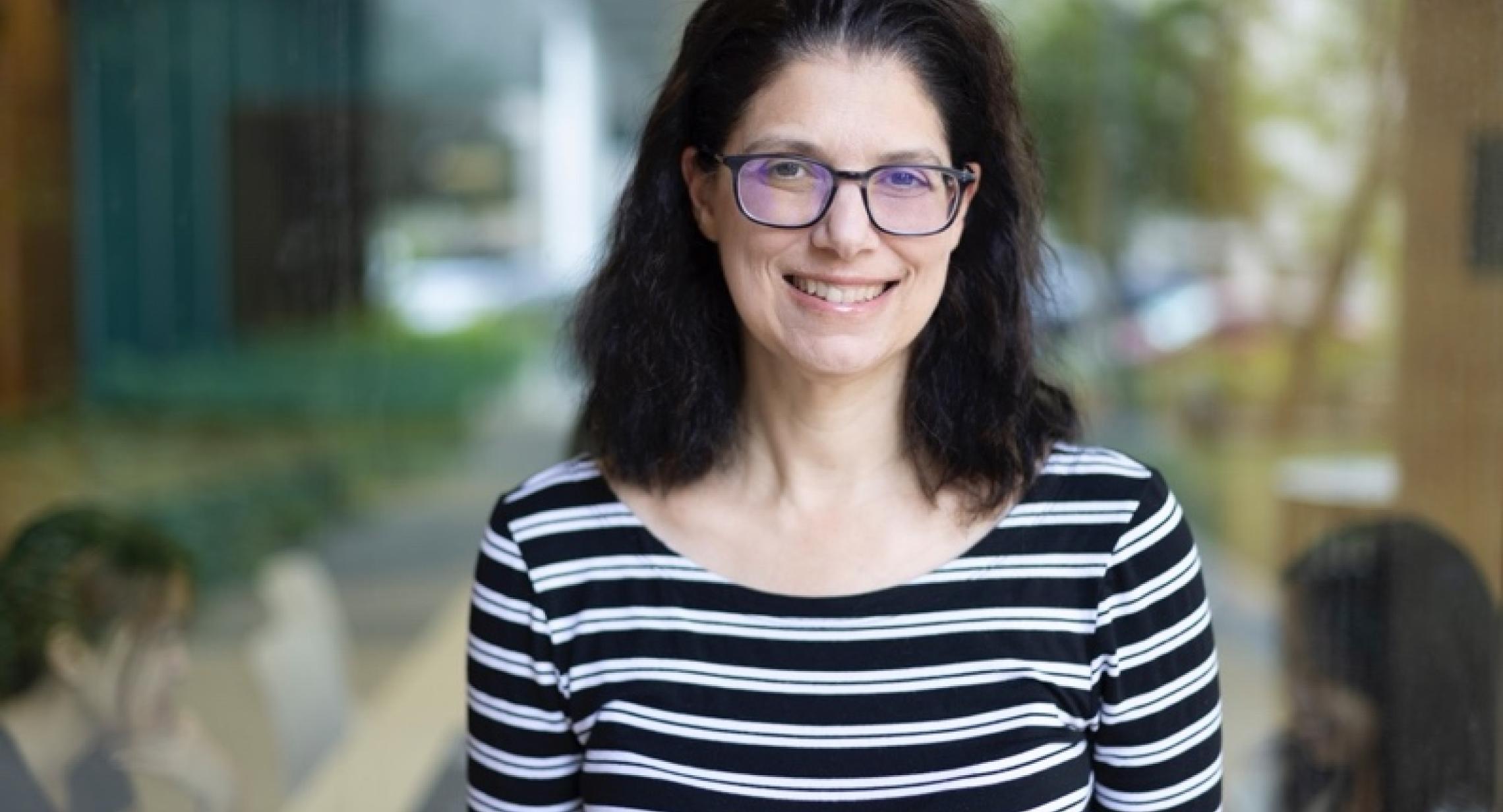 Alisa Perren Profile Picture, black and white stripped shirt, out-of-focus green background, black shoulder length hair and glasses