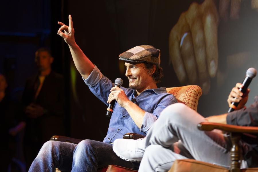 With his arm up in a "hook 'em" hand sign, Matthew McConaughey sits in an armchair during the Q&A portion of the screening event